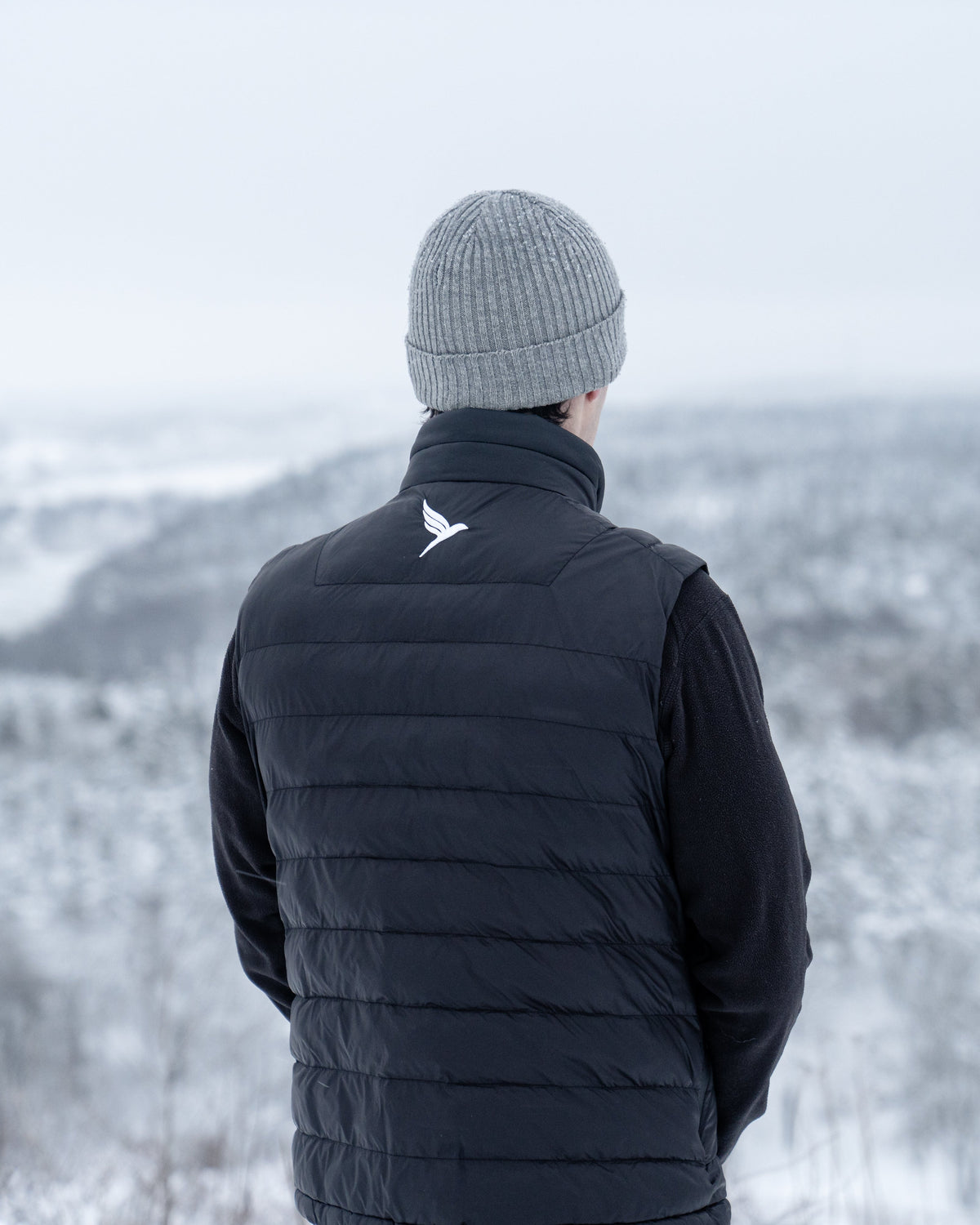 Person wearing a black puffer vest and gray beanie standing in a snowy landscape
