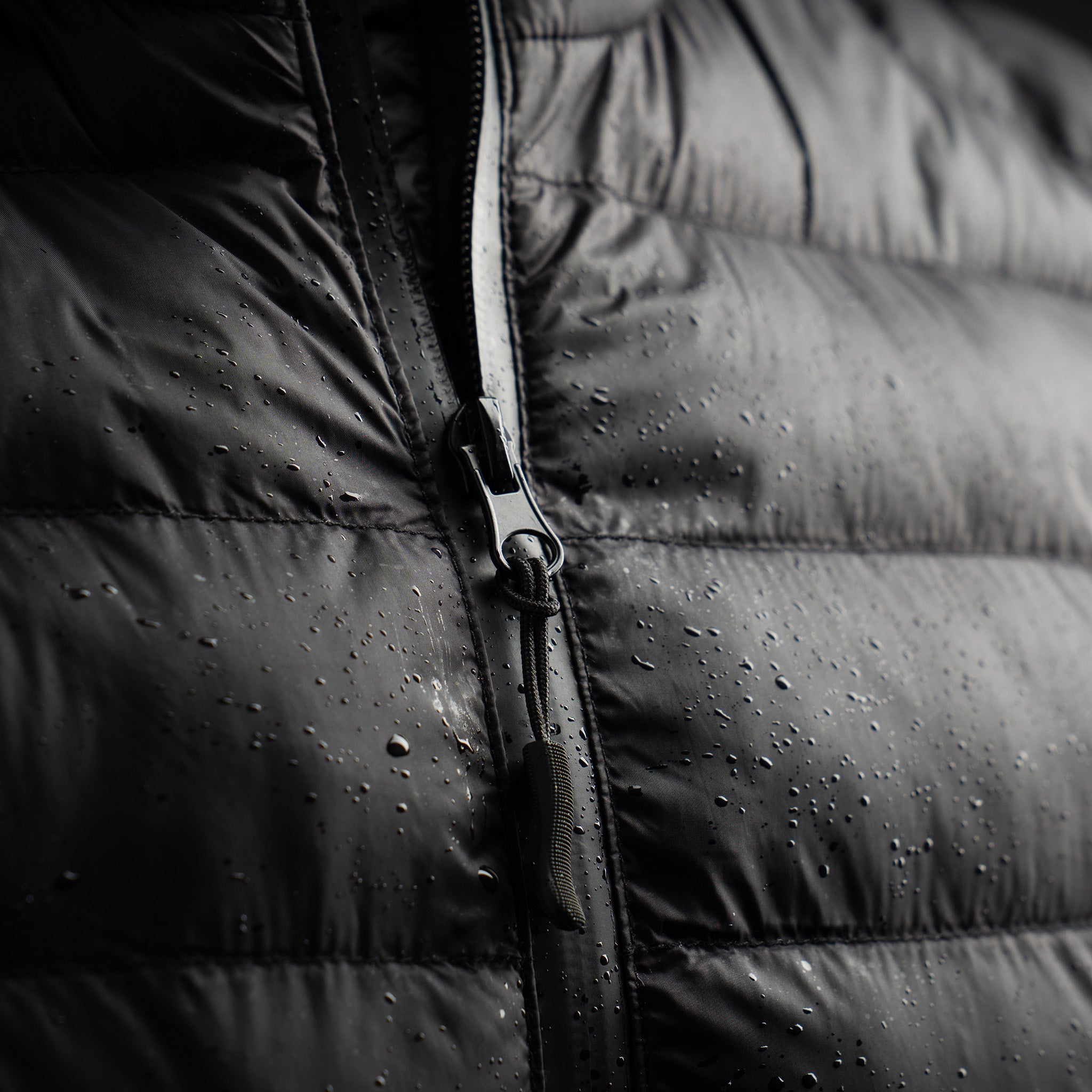 Close-up of a black puffer vest with water droplets on the surface.