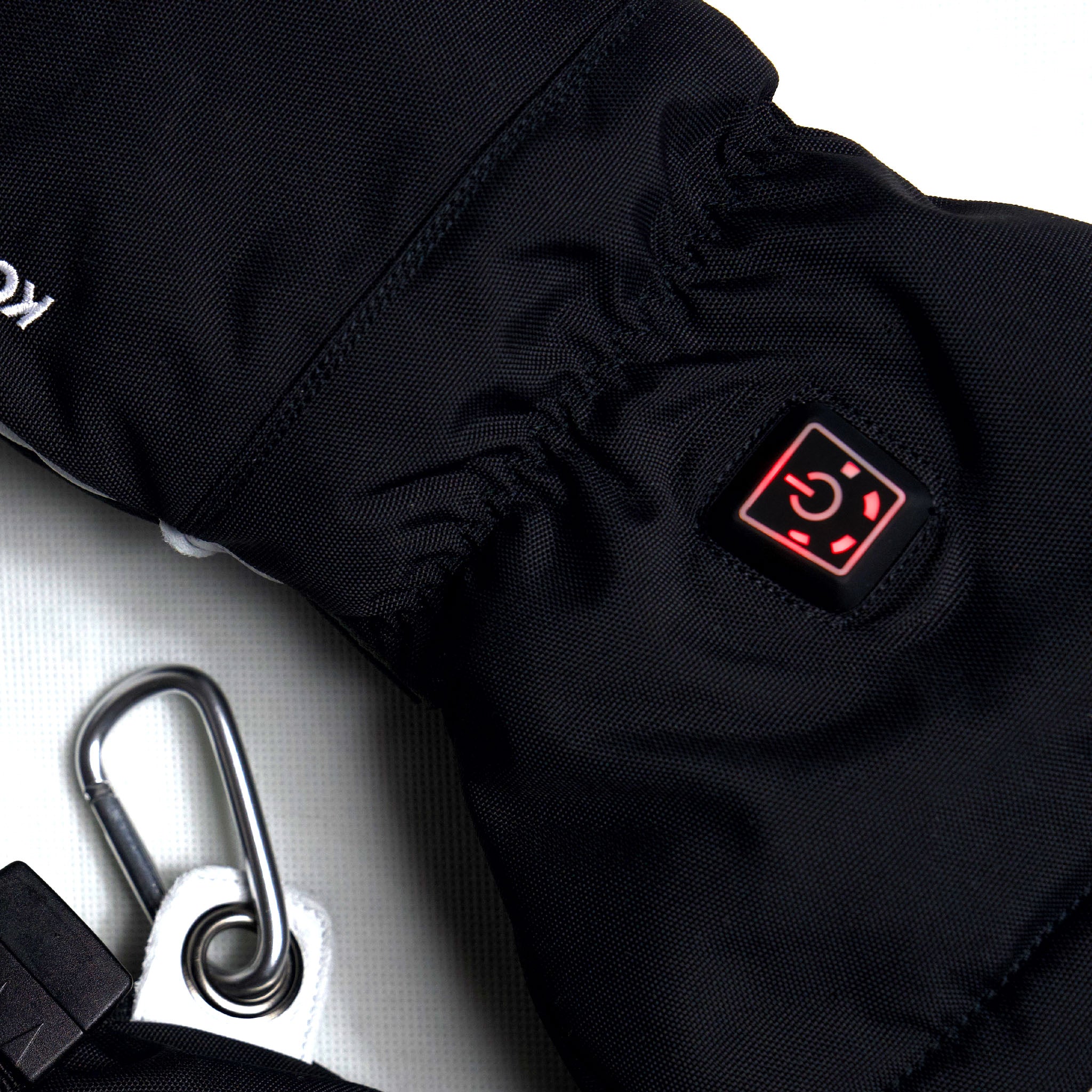 Black heated glove with a red heating indicator next to a silver carabiner on a white background