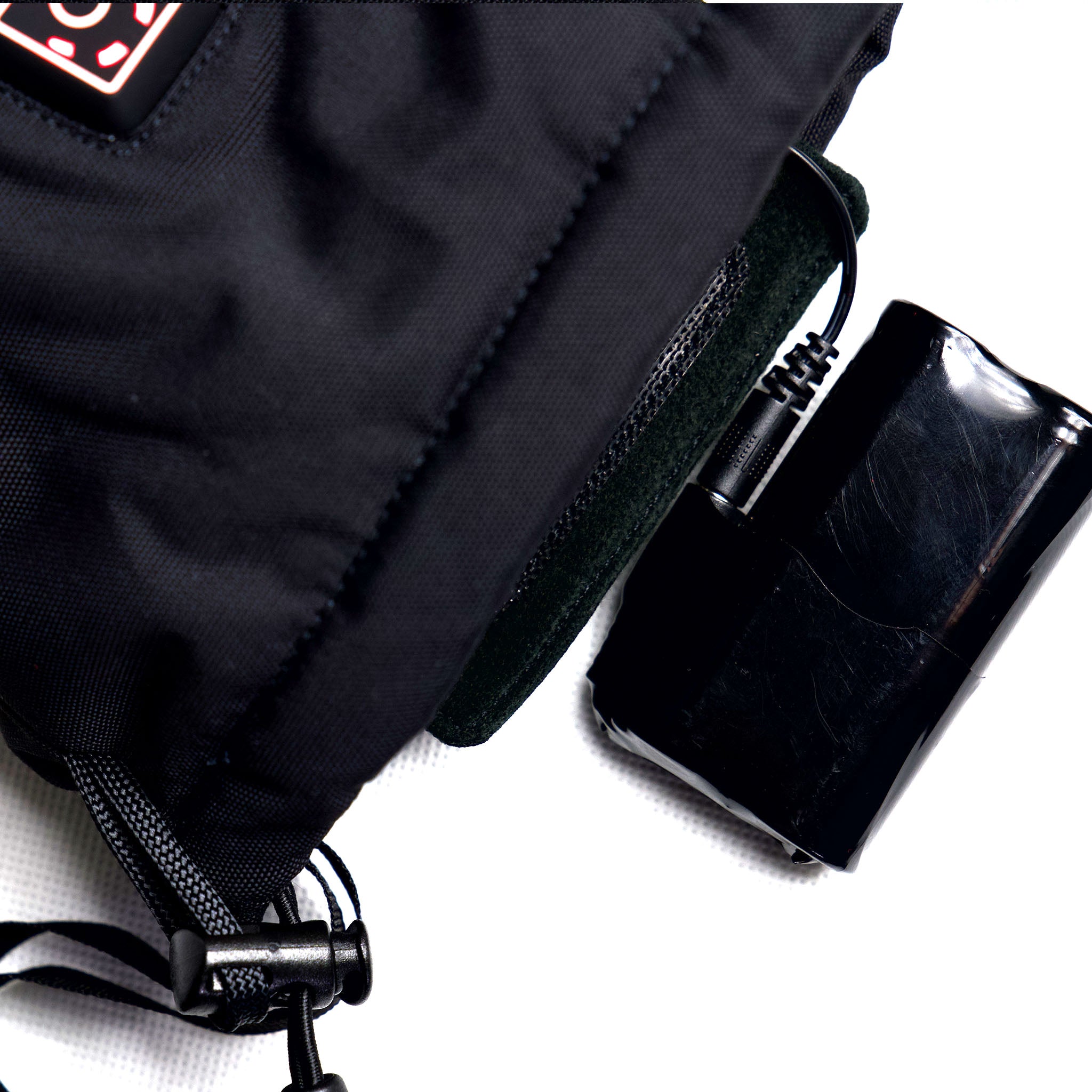 Black battery connected to heated mitten on a white background