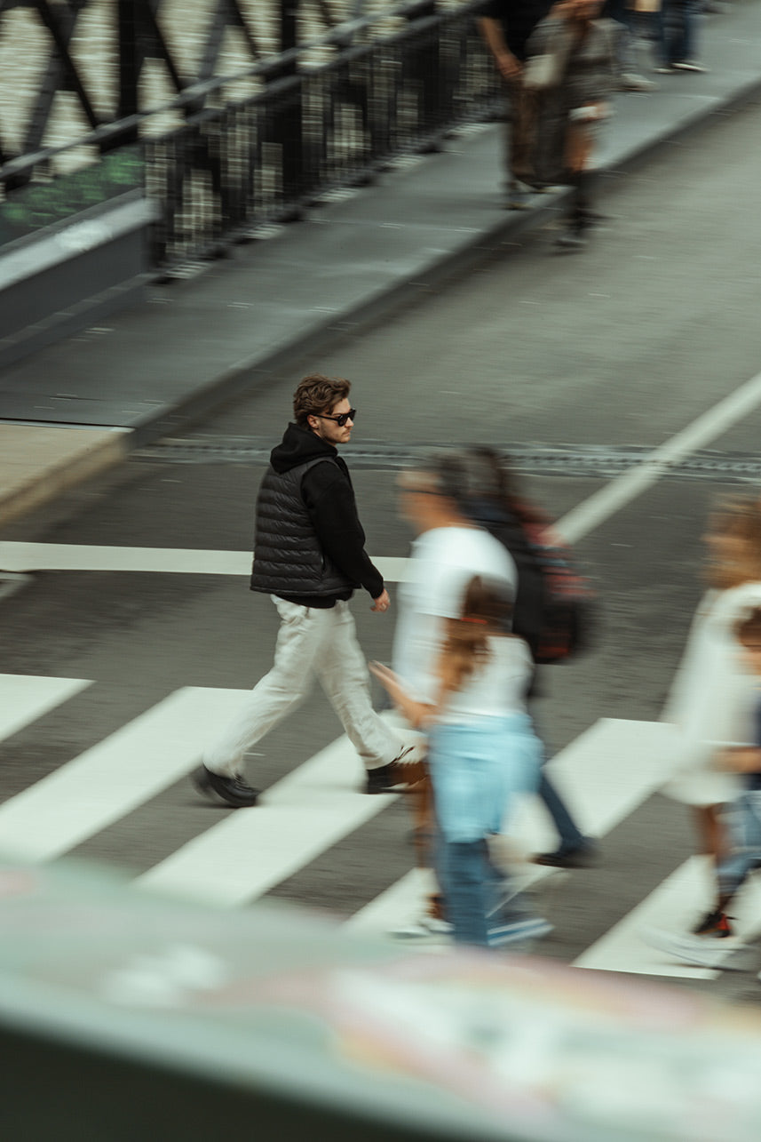 Person in a black vest crossing the street.
