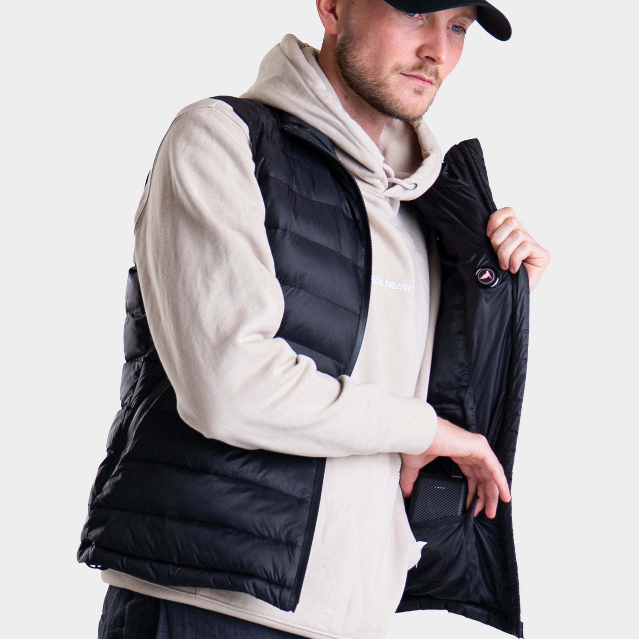 Person wearing a black Koltrast heated vest over a white hoodie on a light gray background