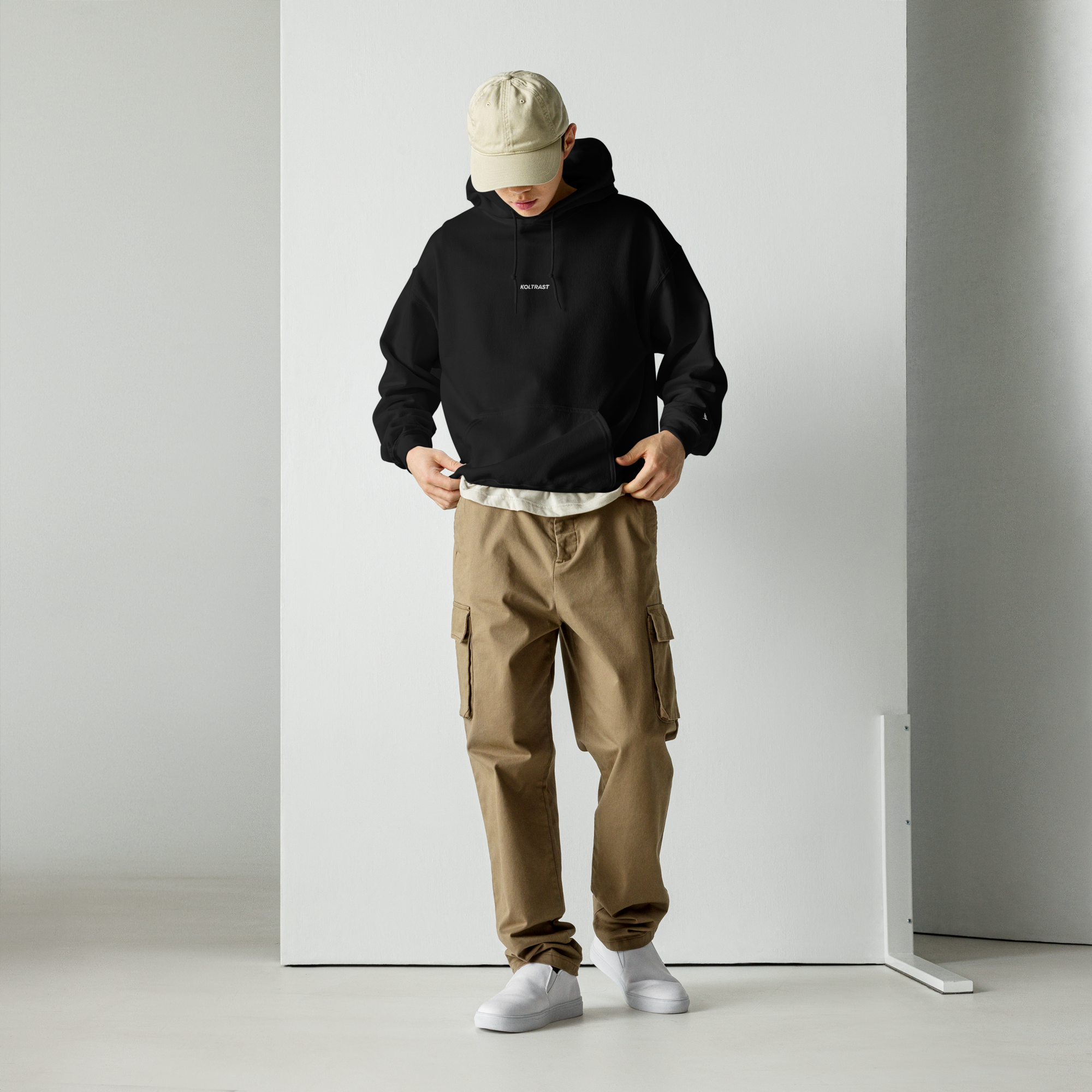 Person wearing a black Koltrast hoodie, beige cap, and brown cargo pants against a white background